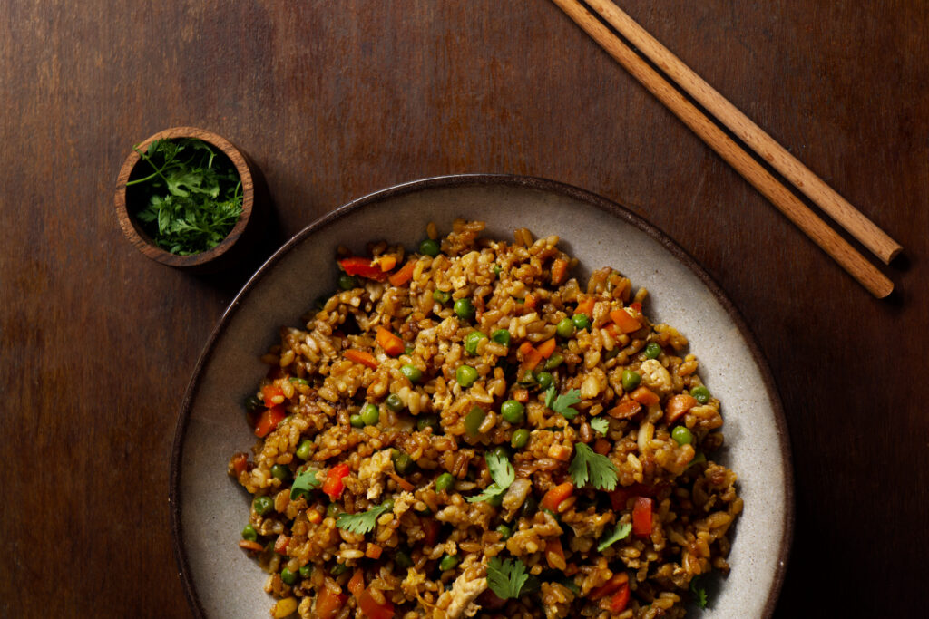 A hearty skillet meal of ground beef and rice with colorful vegetables, served on a rustic wooden table.