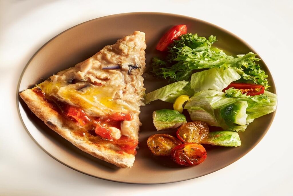 Canned chicken pizza slice paired with Caesar salad and roasted vegetables