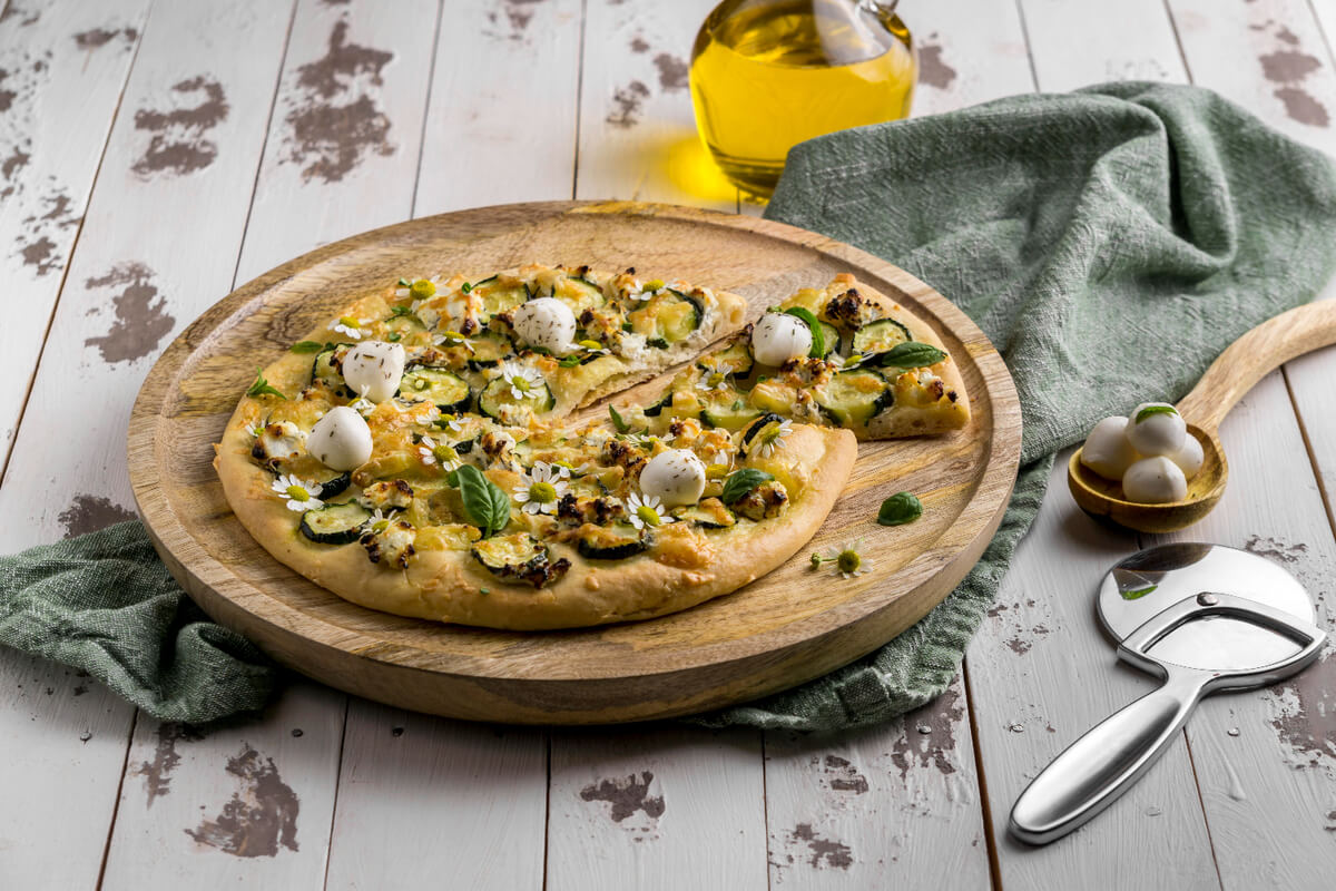 Chicken crust pizza topped with melted cheese, bell peppers, and fresh basil on a wooden board.