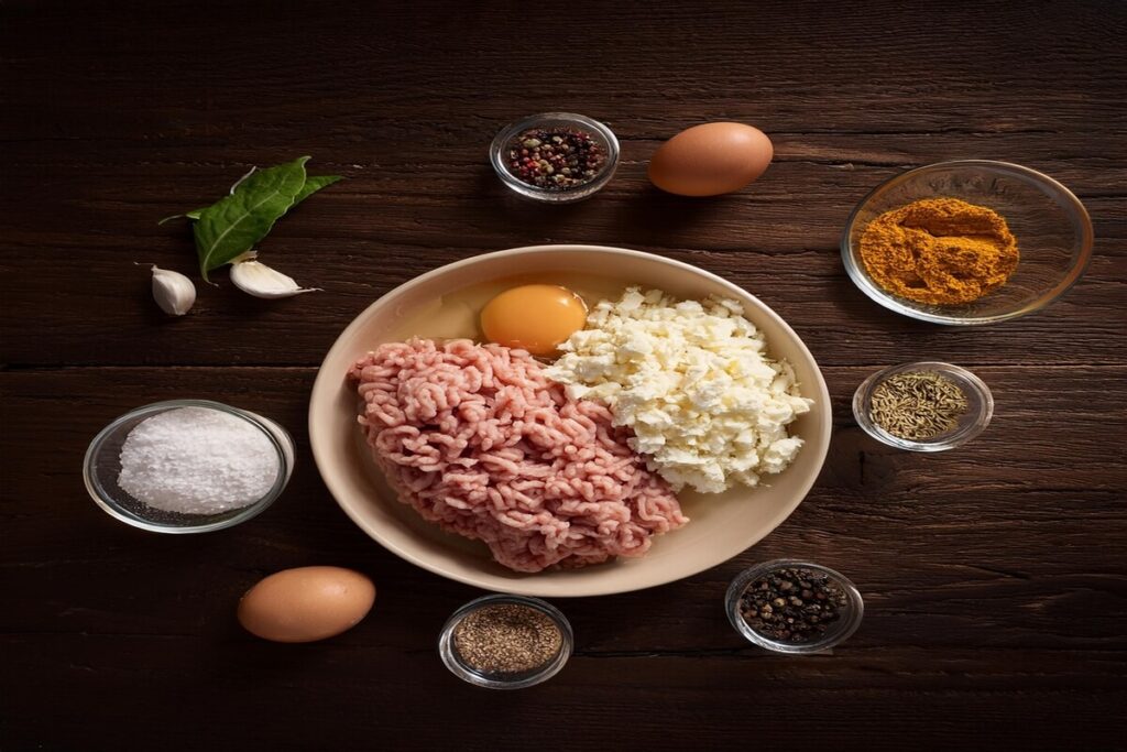 Ground chicken, shredded mozzarella cheese, and an egg on a wooden table—ingredients for chicken crust pizza.