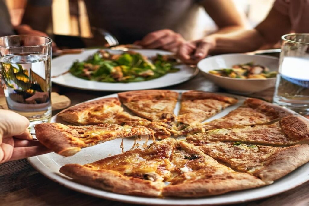 A family sharing slices of chicken crust pizza with salad and drinks on the table.