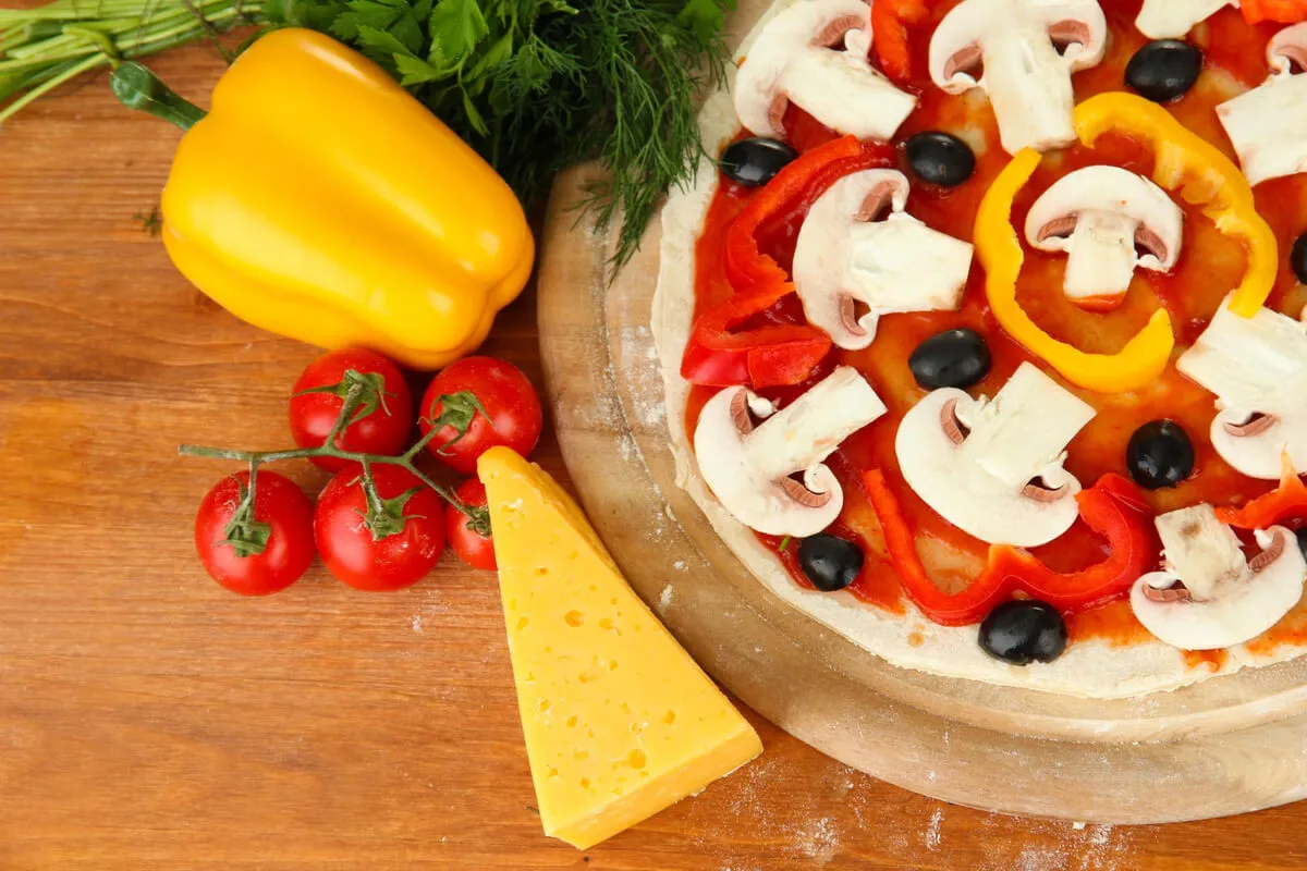 A freshly baked cauliflower crust pizza with colorful toppings on a rustic wooden table.