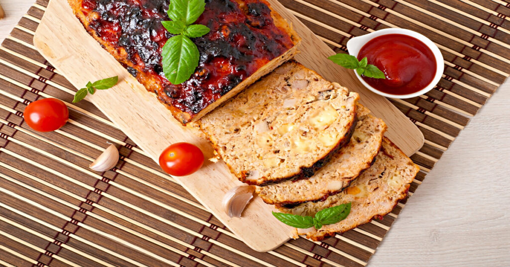 Sliced meatloaf served with mashed potatoes and green beans on a rustic table.