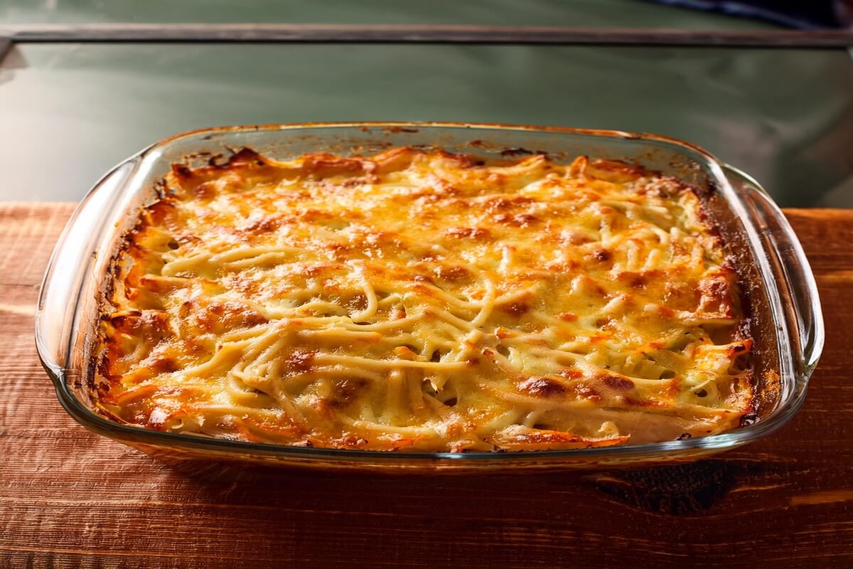 A freshly baked spaghetti casserole topped with golden melted cheese and garnished with parsley, served in a glass dish on a wooden table.