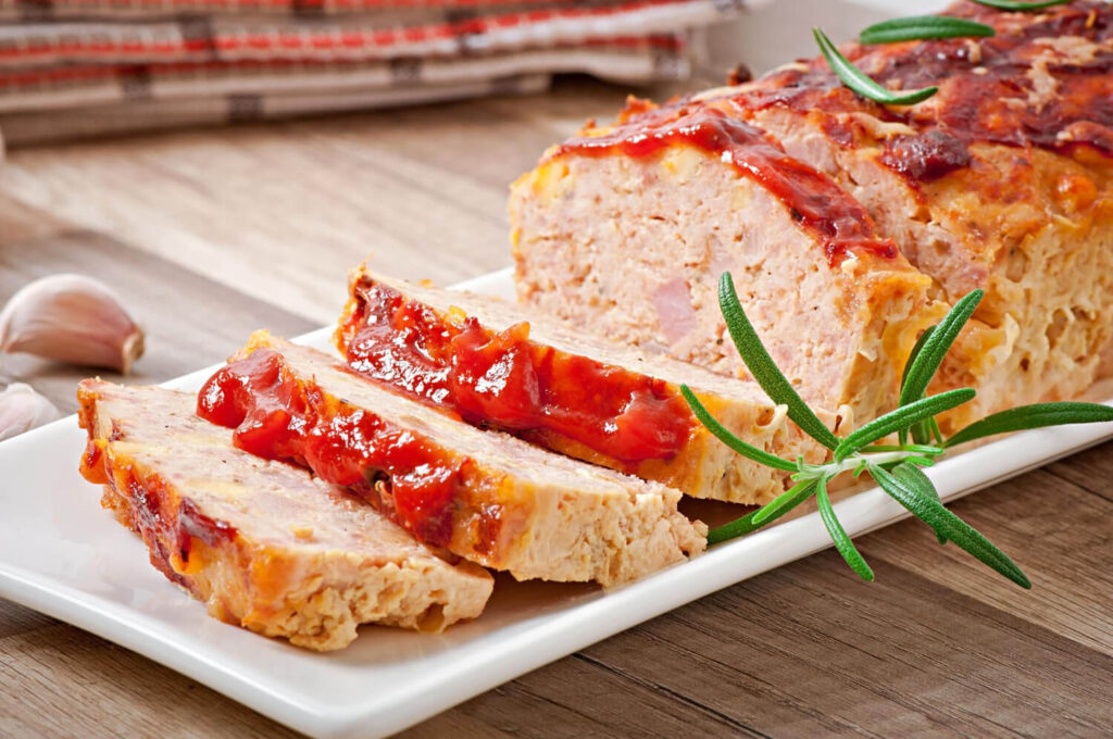 Sliced juicy meatloaf garnished with fresh parsley on a wooden platter.