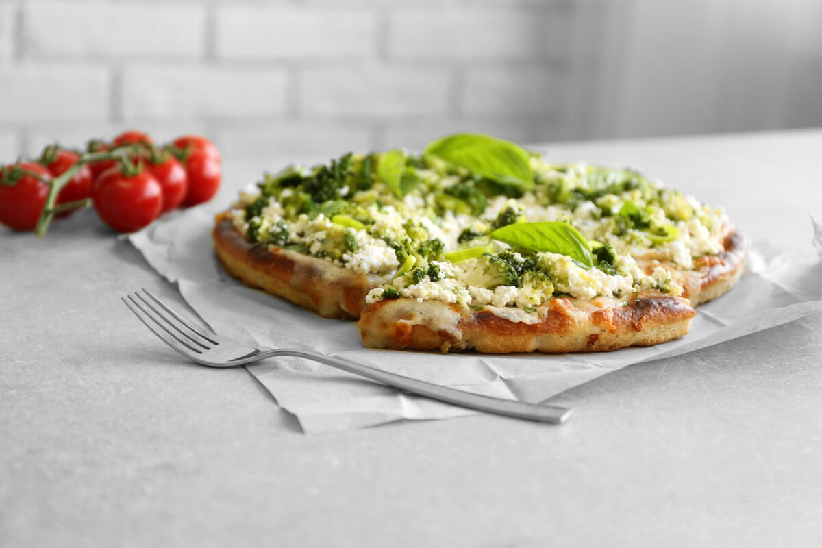 A freshly baked vegan cauliflower pizza crust with fresh basil and vegetables