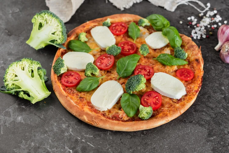 Golden cauliflower pizza crust with cherry tomatoes and arugula on a rustic board.