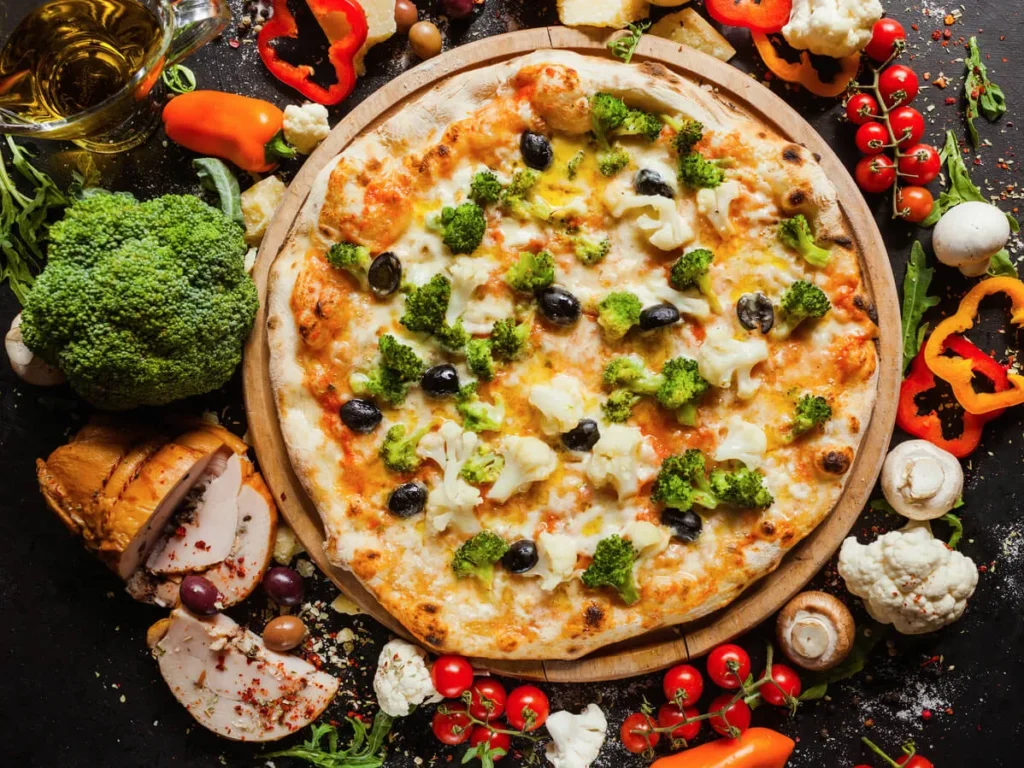 A golden-brown cauliflower pizza crust on a wooden surface with basil leaves.