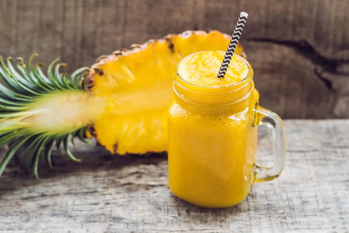 A vibrant Mango Pineapple Smoothie garnished with pineapple and mango slices, set on a rustic table with tropical leaves.